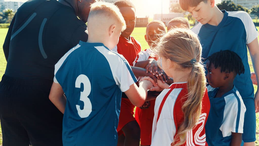 Youth soccer team huddle stacking hands on field